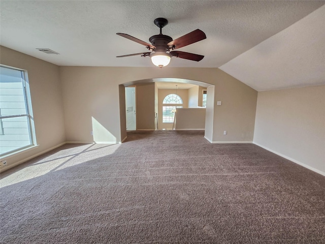 carpeted empty room with visible vents, baseboards, lofted ceiling, arched walkways, and a textured ceiling