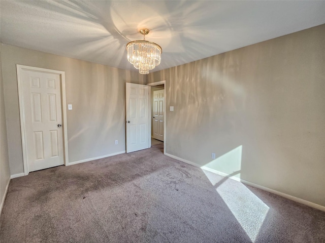 empty room with baseboards, a notable chandelier, and carpet