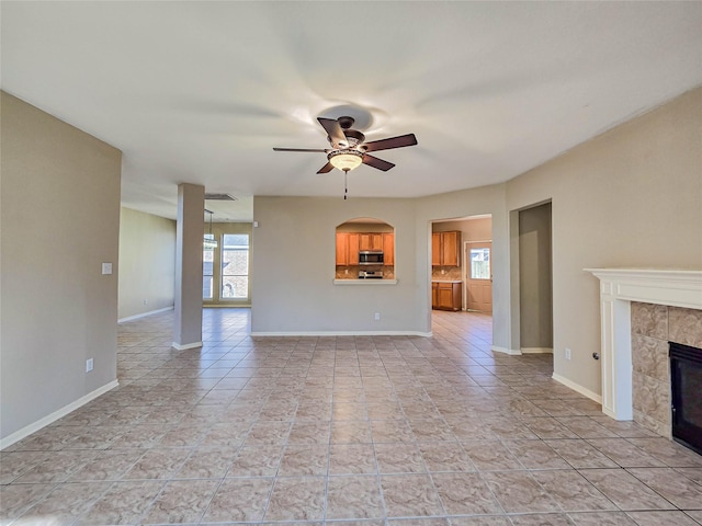 unfurnished living room featuring ceiling fan, plenty of natural light, baseboards, and a tile fireplace