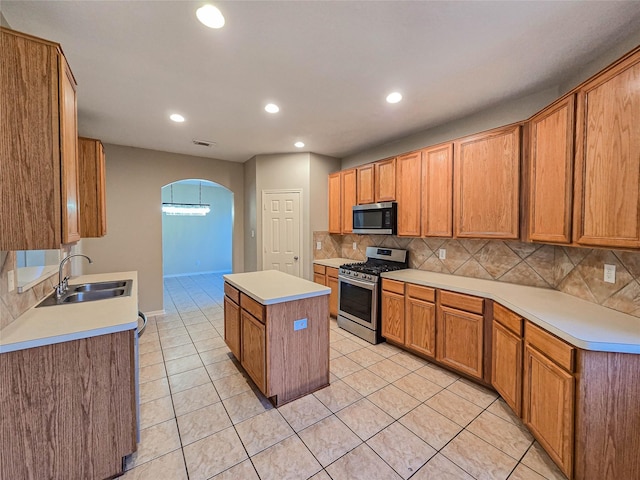 kitchen featuring a kitchen island, light tile patterned floors, arched walkways, stainless steel appliances, and a sink