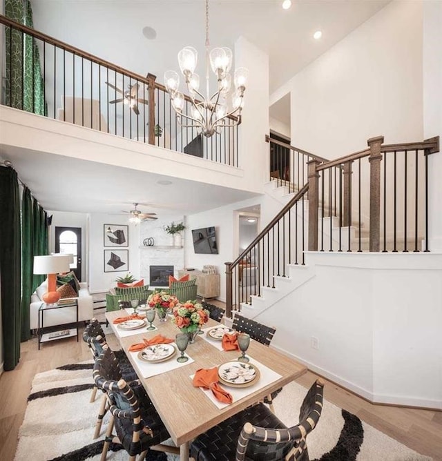 dining area featuring wood finished floors, a glass covered fireplace, stairs, and ceiling fan with notable chandelier