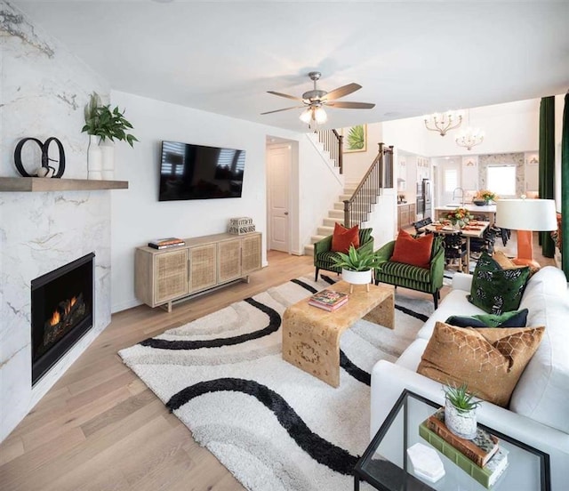 living room featuring light wood finished floors, ceiling fan with notable chandelier, a fireplace, and stairs