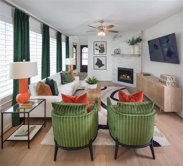 living area featuring ceiling fan, wood finished floors, a healthy amount of sunlight, and a lit fireplace