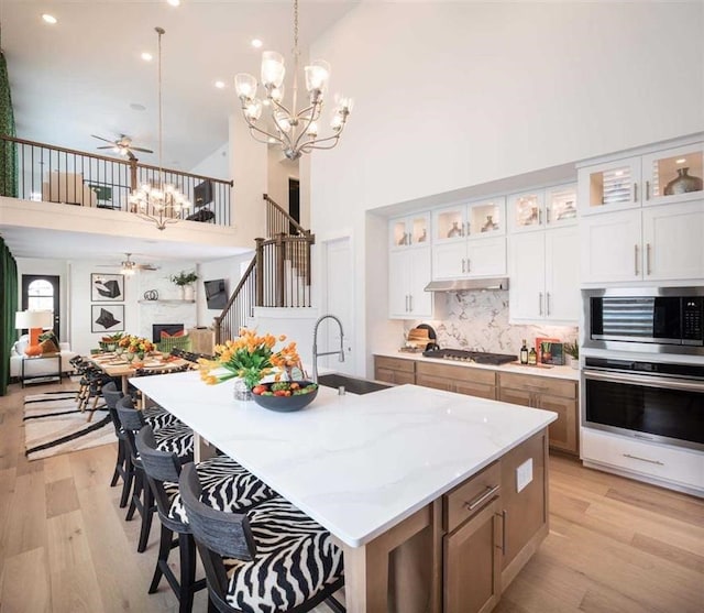 kitchen featuring light wood-style flooring, a sink, under cabinet range hood, appliances with stainless steel finishes, and ceiling fan with notable chandelier