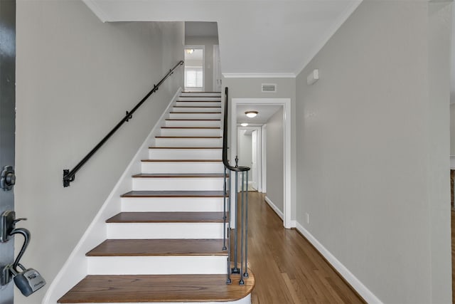 stairway with visible vents, wood finished floors, baseboards, and ornamental molding