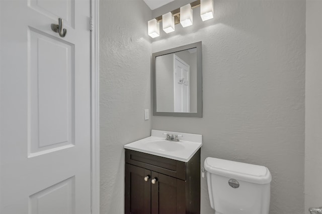 half bathroom featuring vanity, toilet, and a textured wall