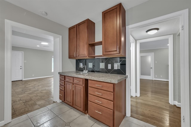 kitchen featuring brown cabinetry, baseboards, open shelves, a sink, and decorative backsplash