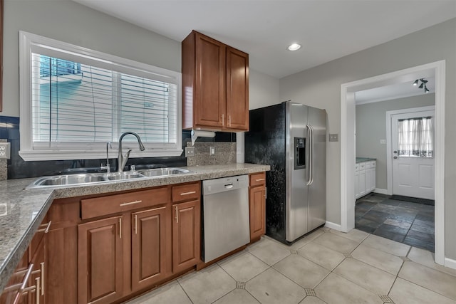 kitchen with brown cabinets, a sink, backsplash, appliances with stainless steel finishes, and baseboards