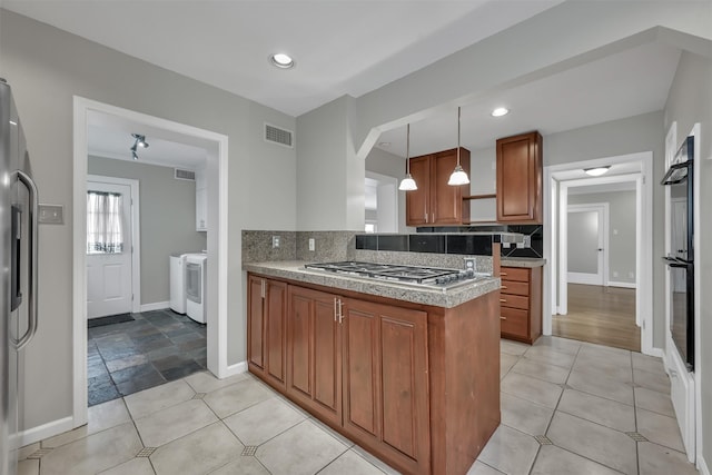 kitchen with brown cabinetry, visible vents, stainless steel appliances, independent washer and dryer, and backsplash