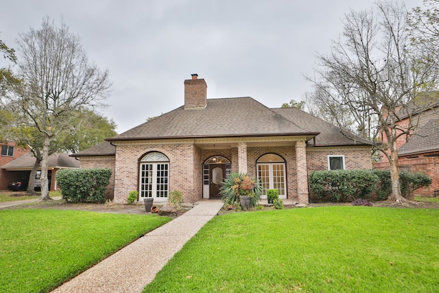 view of front of property with brick siding, french doors, a front yard, and roof with shingles