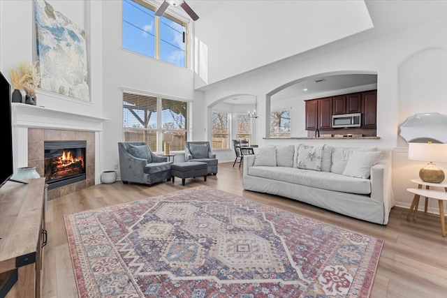 living room featuring light wood finished floors, baseboards, a tile fireplace, an inviting chandelier, and arched walkways