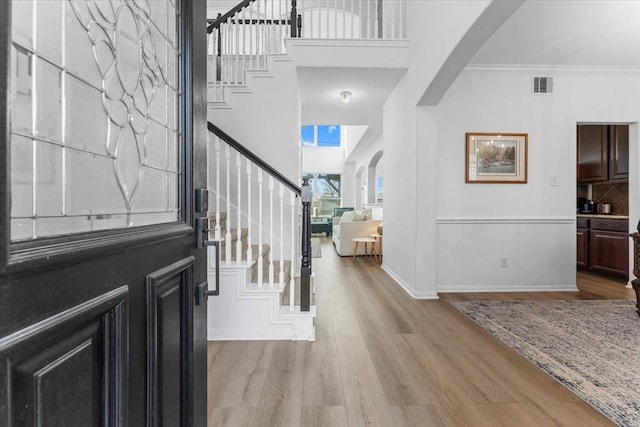 entryway with visible vents, arched walkways, light wood-style floors, and stairs