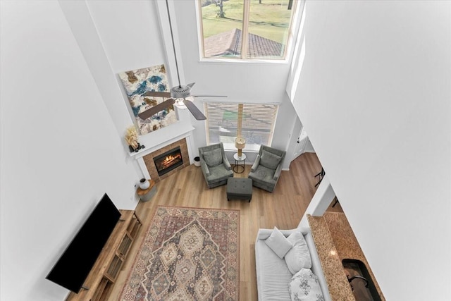 living area with wood finished floors, a high ceiling, a fireplace, and ceiling fan