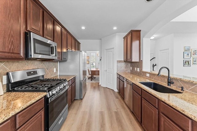 kitchen with appliances with stainless steel finishes, light stone countertops, light wood-type flooring, and a sink