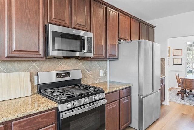 kitchen featuring baseboards, light stone countertops, light wood-type flooring, decorative backsplash, and stainless steel appliances