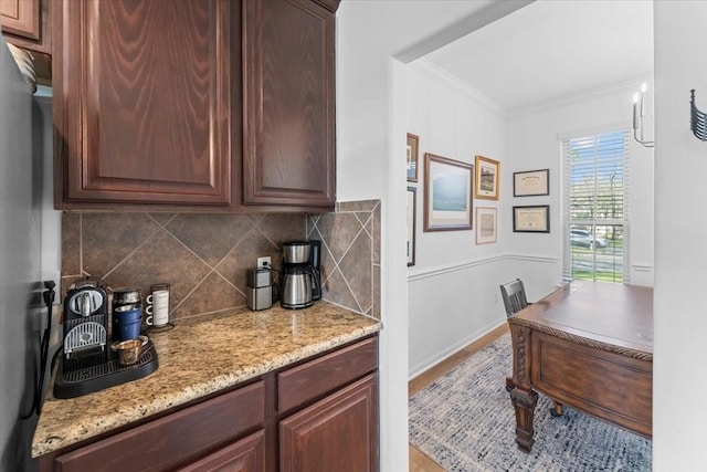 kitchen with light stone countertops, baseboards, dark brown cabinets, crown molding, and backsplash