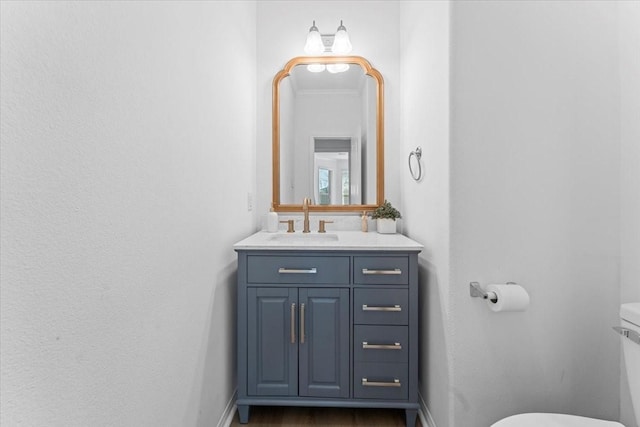 half bathroom with vanity, wood finished floors, baseboards, crown molding, and toilet