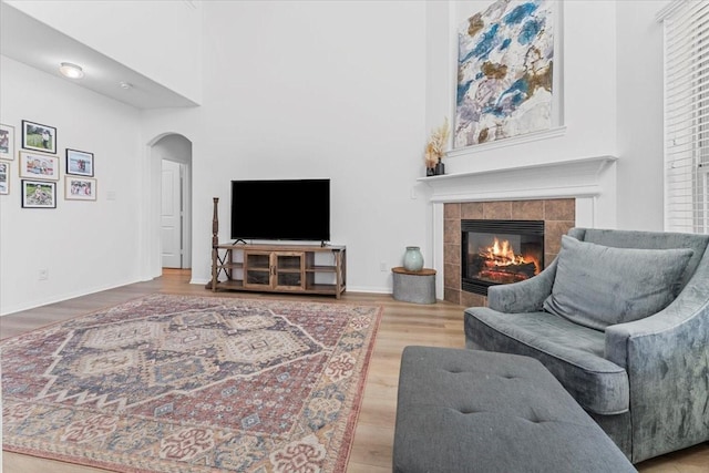 living room featuring baseboards, a tiled fireplace, a high ceiling, wood finished floors, and arched walkways