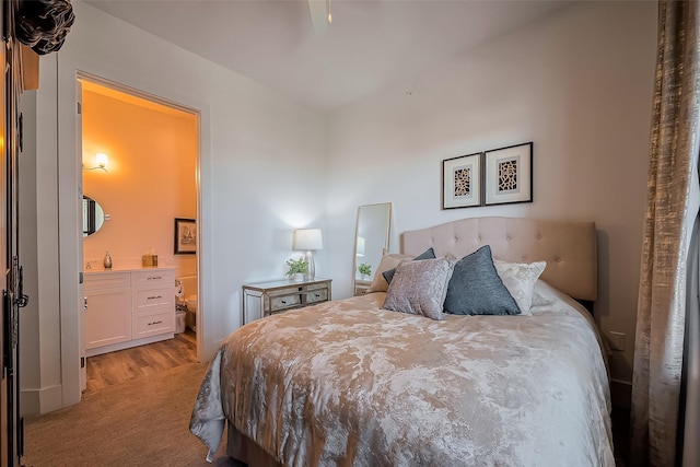 bedroom with connected bathroom, light colored carpet, and light wood-style flooring