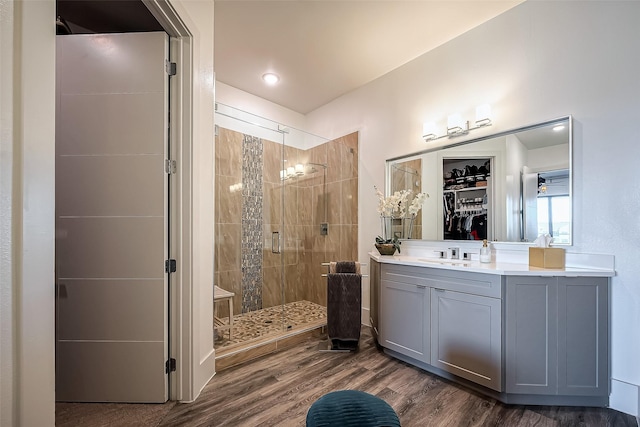 bathroom with a stall shower, vanity, a walk in closet, and wood finished floors