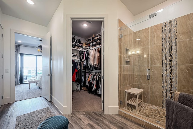 full bath featuring a stall shower, a walk in closet, baseboards, and wood finished floors