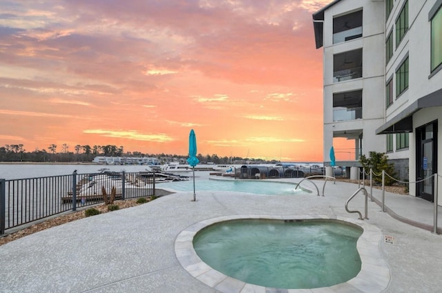 community pool featuring a water view, a patio, a community hot tub, and fence