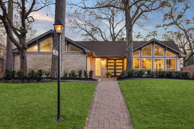 mid-century home featuring a yard, brick siding, and roof with shingles