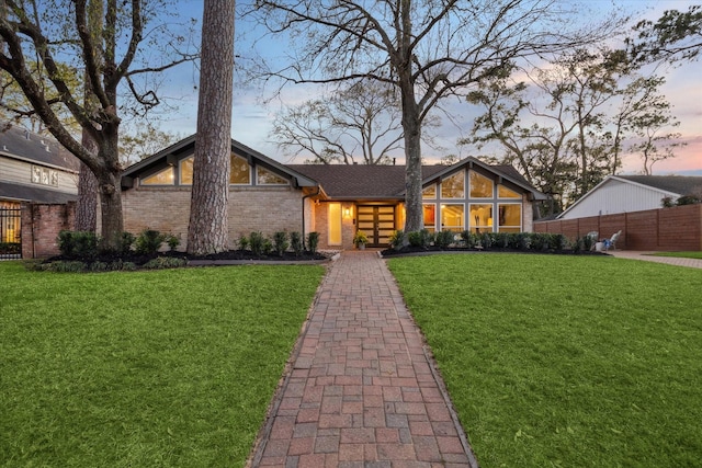 mid-century modern home featuring brick siding, a lawn, and fence