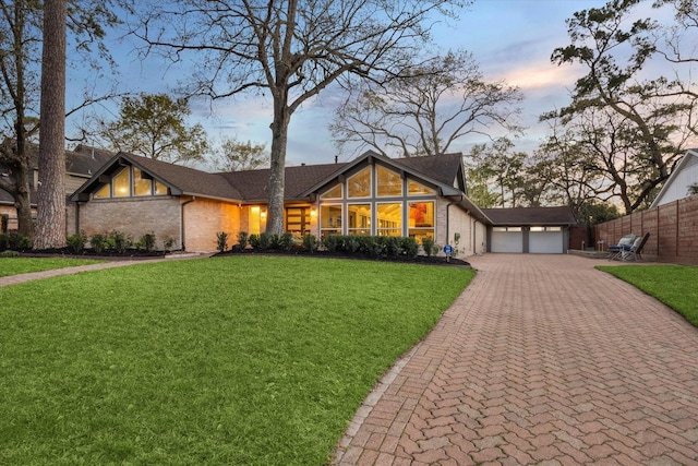 view of front facade featuring a lawn, decorative driveway, fence, a garage, and brick siding