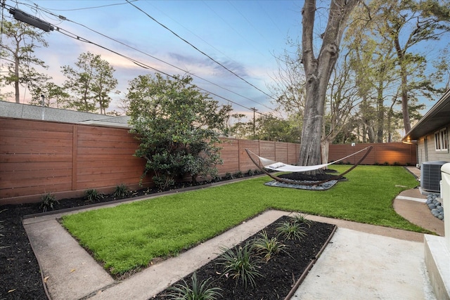 yard at dusk with central AC unit and a fenced backyard