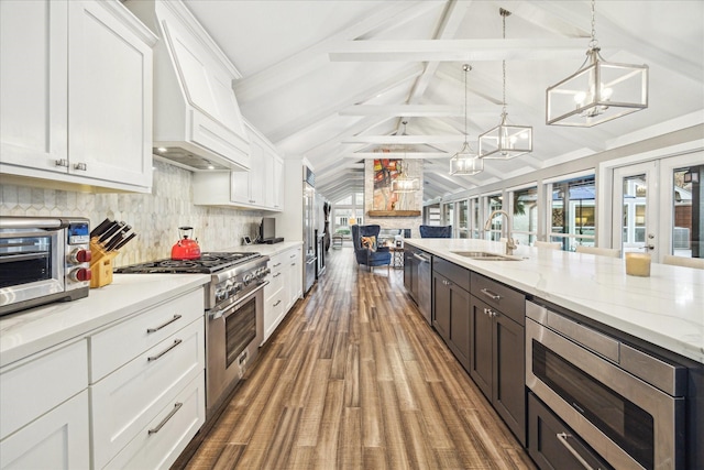 kitchen with appliances with stainless steel finishes, custom exhaust hood, a notable chandelier, white cabinets, and a sink