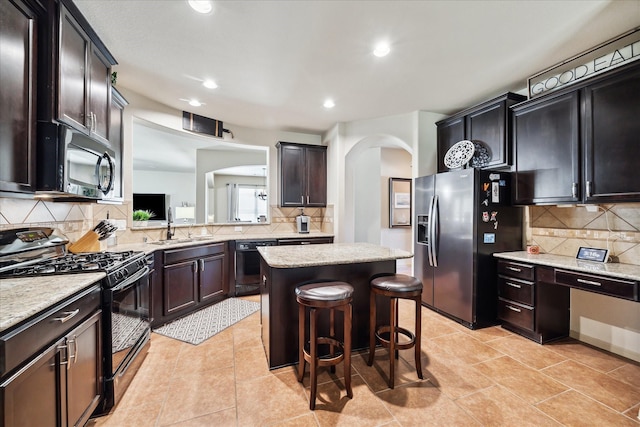 kitchen with a center island, light tile patterned floors, arched walkways, black appliances, and a sink