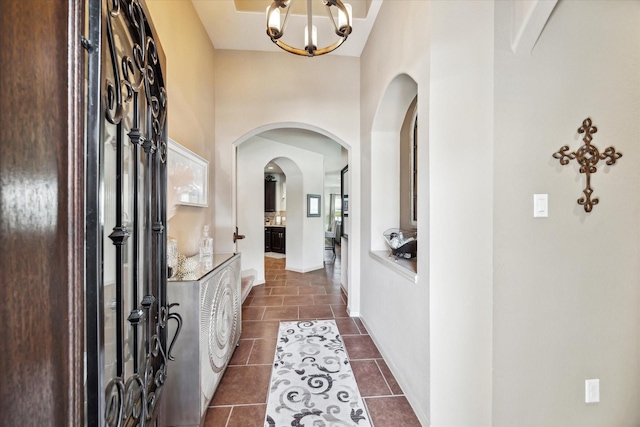 foyer featuring arched walkways, a notable chandelier, dark tile patterned floors, and a towering ceiling