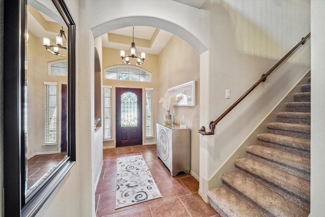 tiled foyer featuring baseboards, a tray ceiling, a high ceiling, stairs, and a notable chandelier