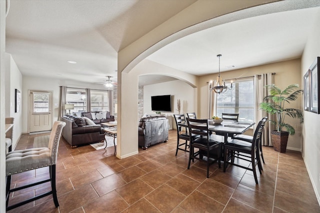 dining area featuring baseboards, arched walkways, dark tile patterned floors, and ceiling fan with notable chandelier