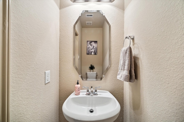 bathroom with a sink, visible vents, and a textured wall