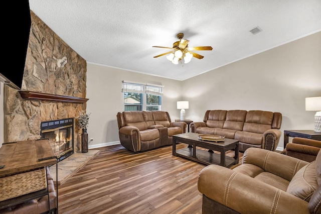 living room with visible vents, ornamental molding, a stone fireplace, wood finished floors, and a textured ceiling