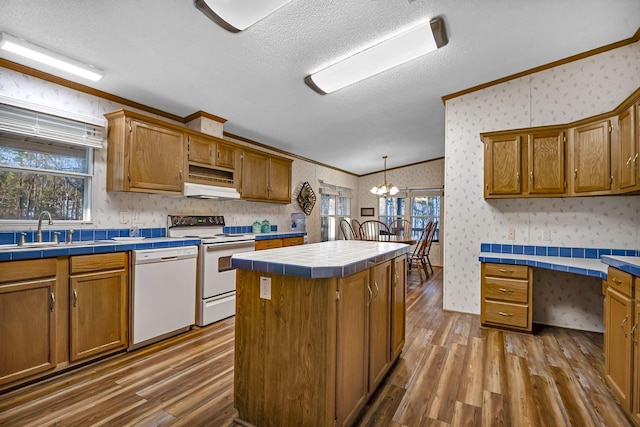 kitchen with white appliances, tile countertops, wallpapered walls, a sink, and crown molding