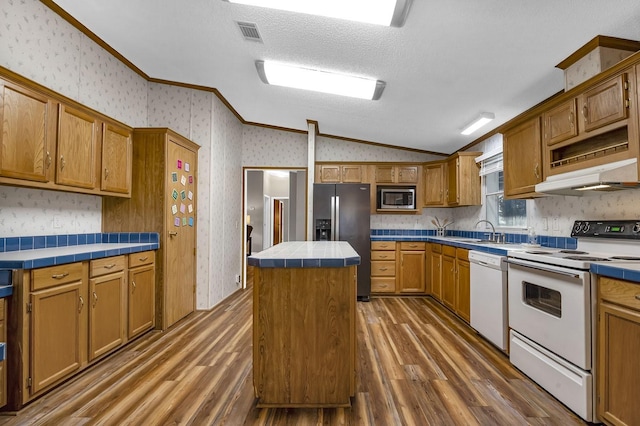 kitchen featuring a center island, appliances with stainless steel finishes, wallpapered walls, tile counters, and vaulted ceiling