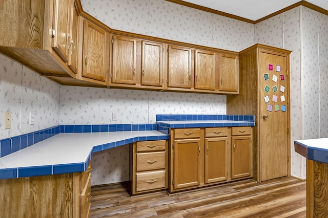 kitchen with brown cabinetry, built in study area, wallpapered walls, and wood finished floors