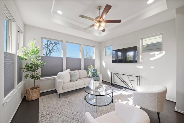 living area with wood finished floors, baseboards, a tray ceiling, recessed lighting, and crown molding