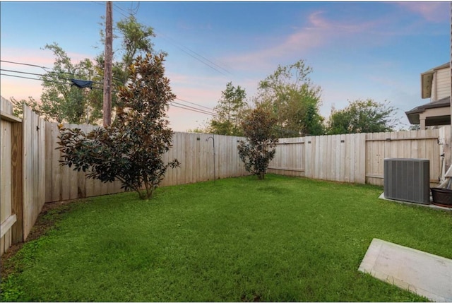 yard at dusk featuring a fenced backyard and central AC