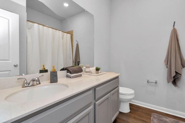 bathroom with toilet, vanity, baseboards, and wood finished floors