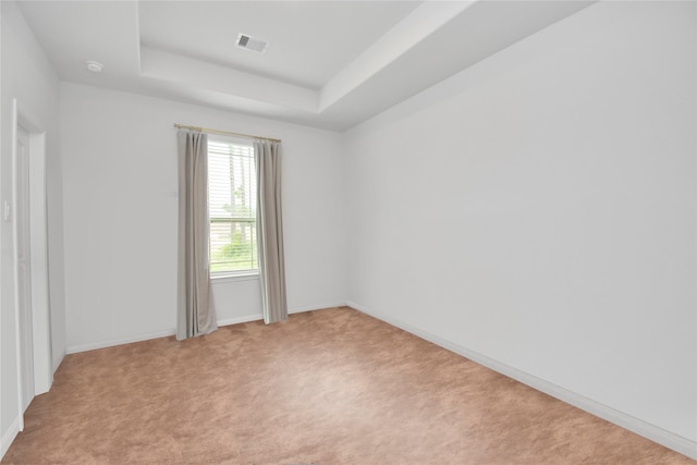 empty room with baseboards, a tray ceiling, light carpet, and visible vents