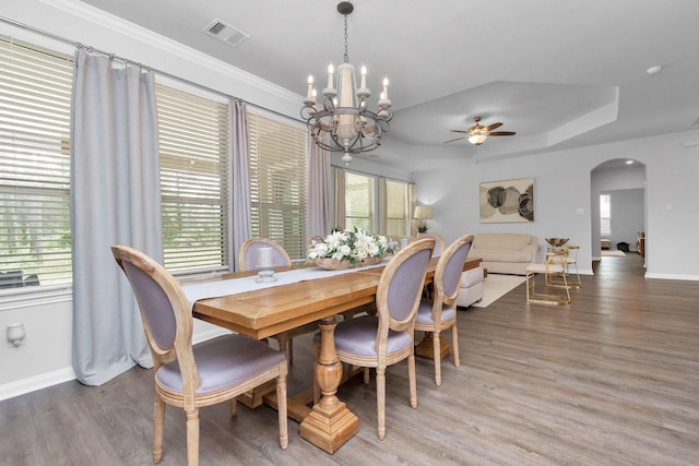 dining area featuring visible vents, plenty of natural light, arched walkways, light wood finished floors, and a raised ceiling