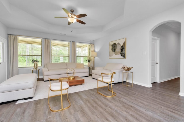 living area featuring baseboards, a raised ceiling, arched walkways, and wood finished floors