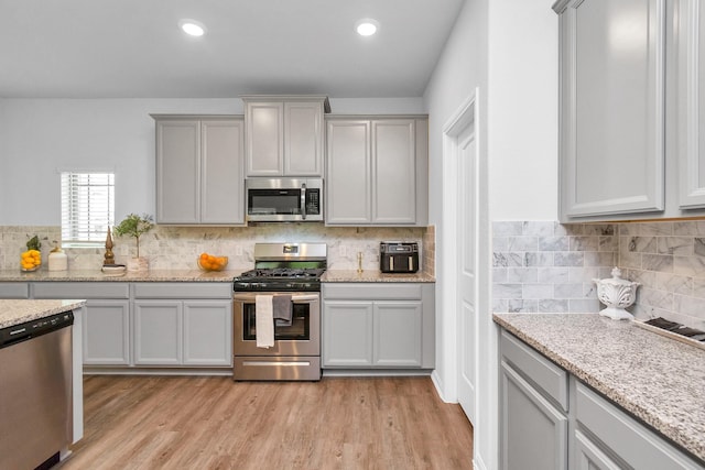 kitchen featuring gray cabinets, tasteful backsplash, recessed lighting, stainless steel appliances, and light wood finished floors