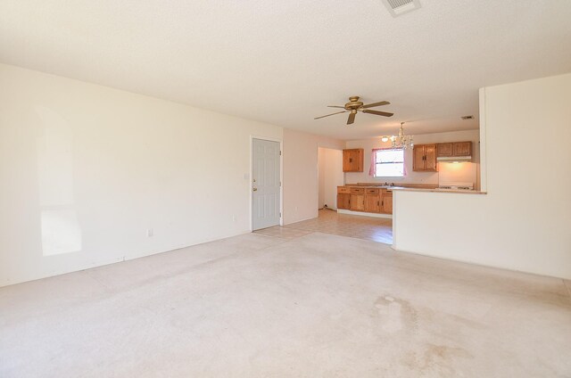 unfurnished living room featuring a sink, ceiling fan with notable chandelier, visible vents, and a textured ceiling