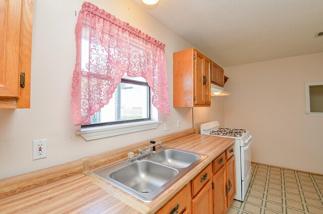 kitchen featuring white range with gas cooktop, a sink, light countertops, under cabinet range hood, and a textured ceiling