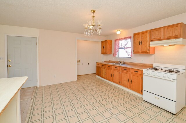 kitchen with under cabinet range hood, a sink, gas range gas stove, light countertops, and light floors